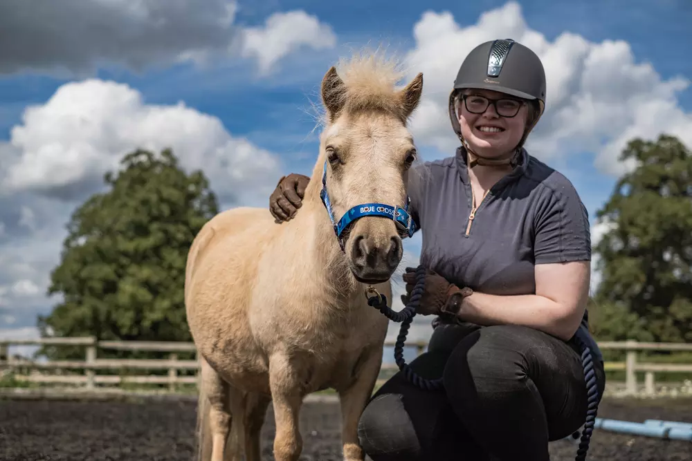 Golden-coloured Shetland pony Megan is embraced by her smiling rehomer