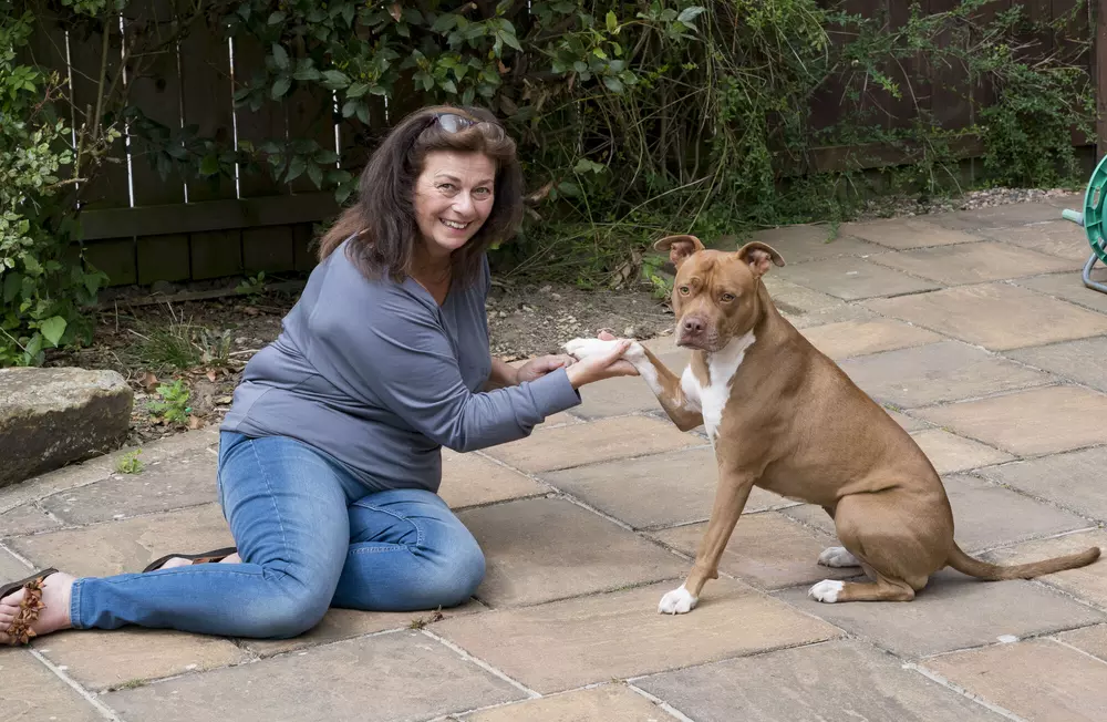 Anita holding Lola's right paw with both sitting on concrete looking to camera