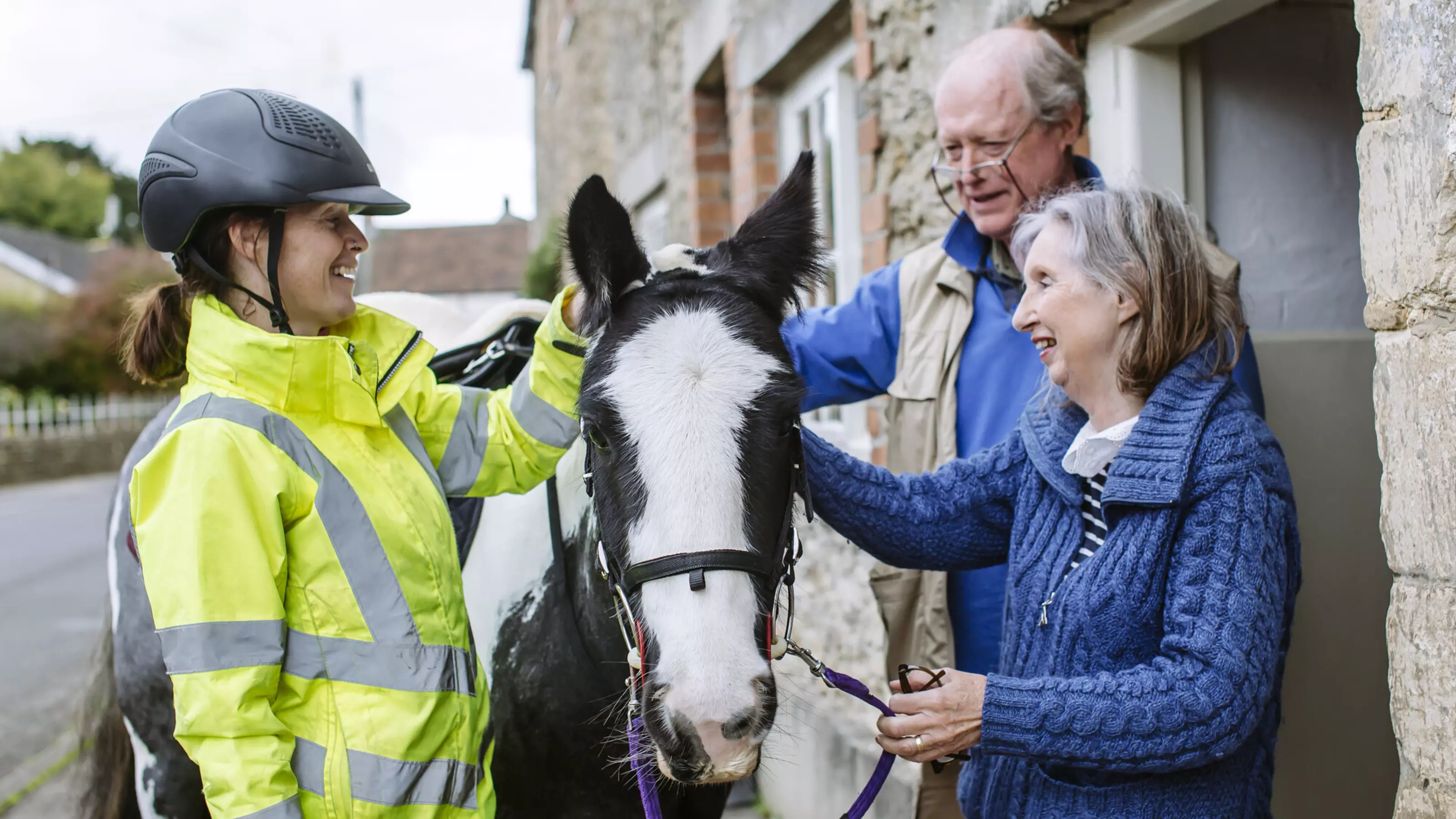 Black and white horse is stroked by woman and man outside their home